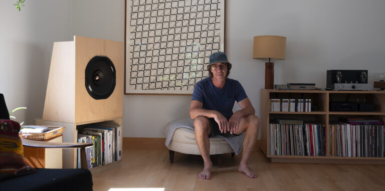 A person sits on an ottoman surrounded by personal artifacts.